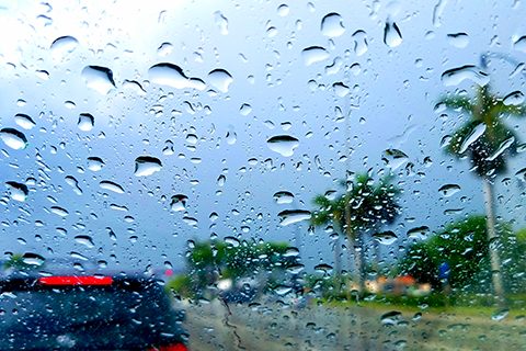 This is a stock photo from Shutterstock. The image focuses on the raindrops on a car window. The car is stuck in traffic in Miami.